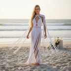 Woman in a white fringe dress standing on a beach with ocean in the background