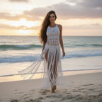 Woman in a white macramé dress walking on a beach at sunset.